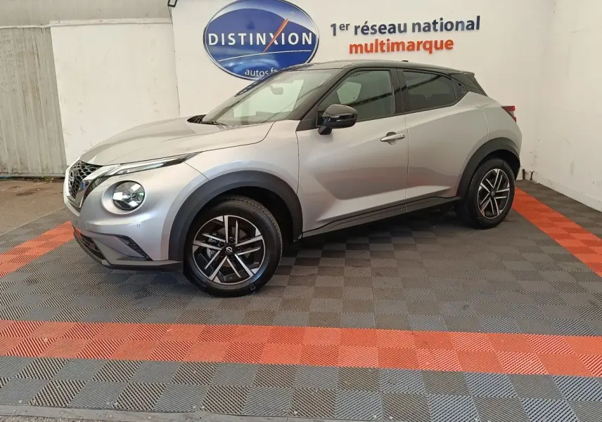 Vue de profil droit d'un Nissan Juke gris clair 2025 avec jantes alliage et toit noir dans un showroom.