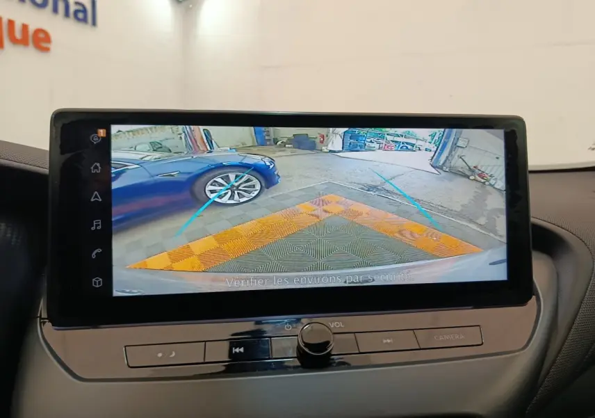 Écran tactile intérieur montrant la caméra de recul avec vue arrière sur un sol et une voiture bleue à gauche.