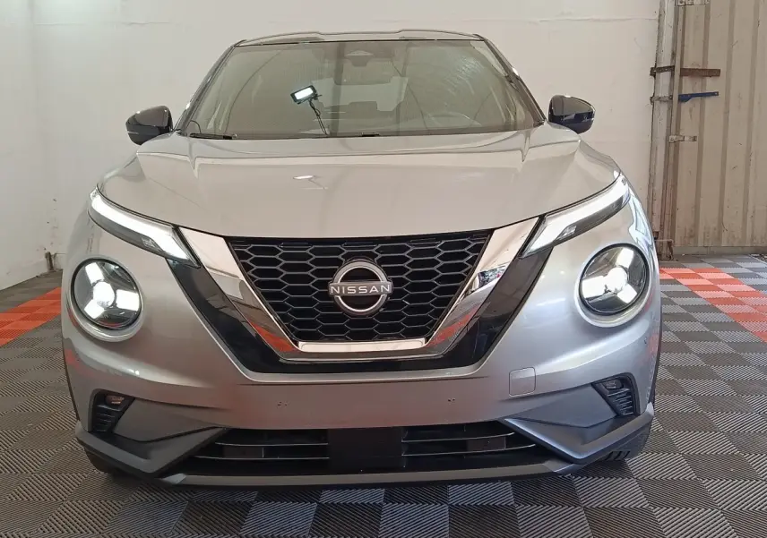 Vue frontale d'un Nissan Juke gris clair 2025 avec phares LED ronds et calandre en V chromée.