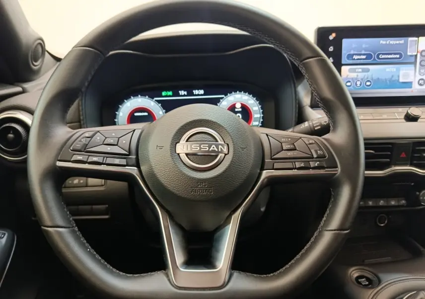 Vue rapprochée du volant noir multifonctions et du tableau de bord numérique du Nissan Juke 2025 essence gris clair.