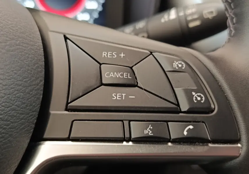Gros plan sur les commandes du régulateur de vitesse et téléphone au volant du Nissan Juke gris clair 2025.