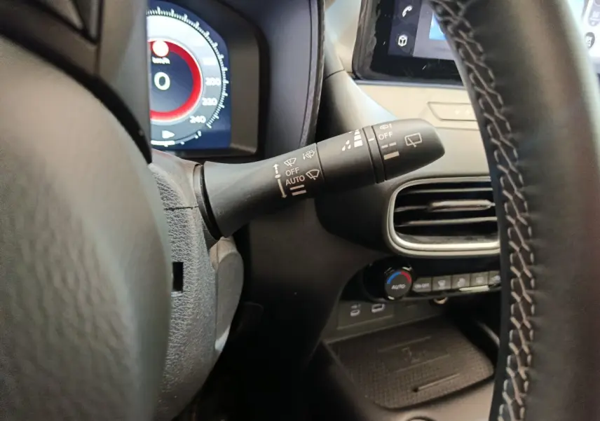 Gros plan sur le commodo d’essuie-glace à gauche du volant du Nissan Juke gris clair, avec tableau de bord et écran tactile en arrière-plan.