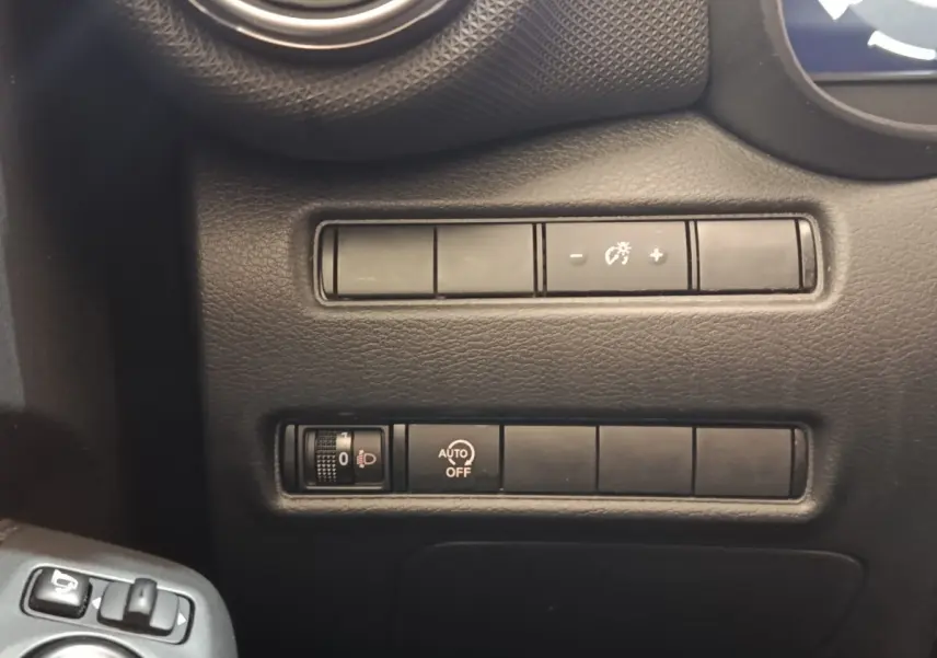 Gros plan sur les commandes de réglage des phares et luminosité du tableau de bord d'un Nissan Juke gris clair.