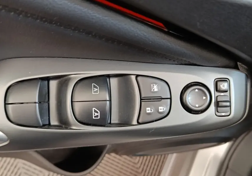 Gros plan sur les commandes de lève-vitres et rétroviseurs côté conducteur d’un Nissan Juke 2025 gris clair.