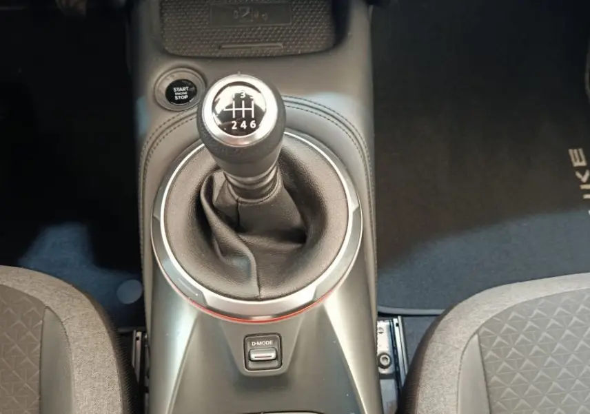 Vue intérieure centrée sur la console centrale du Nissan Juke gris clair, mettant en valeur le levier de vitesse manuel et les commandes.