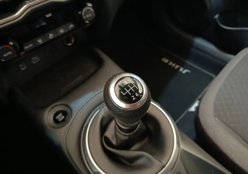 Gros plan sur le levier de vitesse manuel noir du Nissan Juke gris clair, avec tapis marqué "JUKE" visible côté passager.