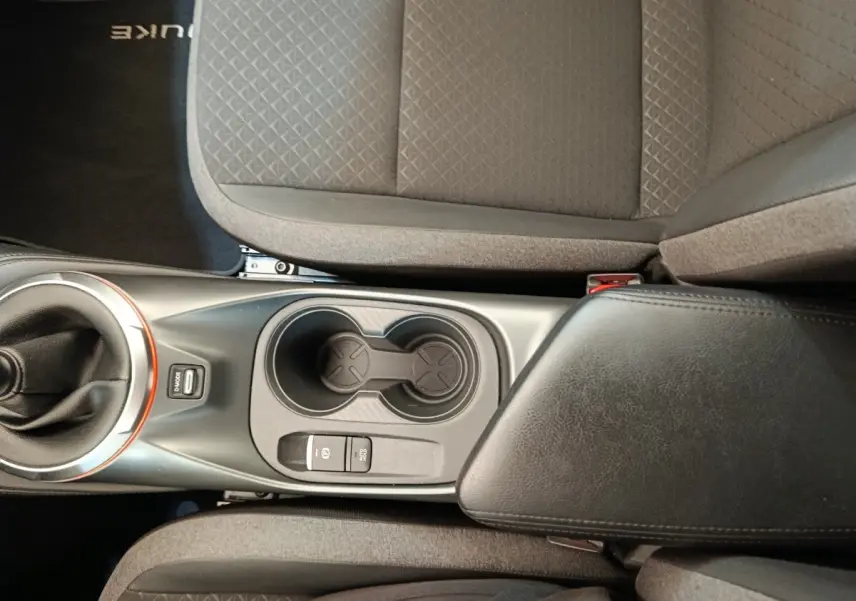 Vue plongeante sur la console centrale noire avec levier de vitesse et accoudoir en cuir du Nissan Juke gris clair 2025.