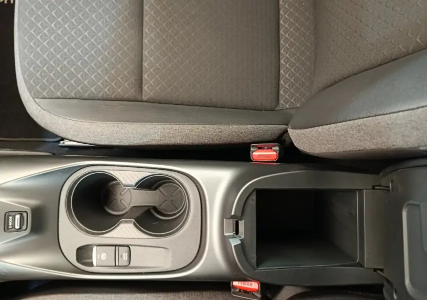 Vue plongeante sur la console centrale noire avec porte-gobelets et accoudoir ouvert du Nissan Juke gris clair.
