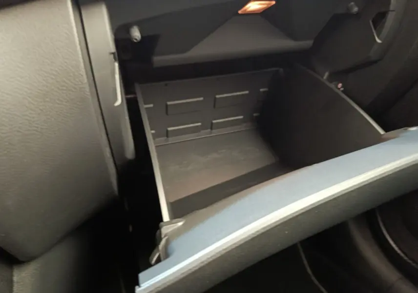 Gros plan sur la boîte à gants ouverte côté passager du Nissan Juke gris clair, montrant l'intérieur vide et la texture du tableau de bord.