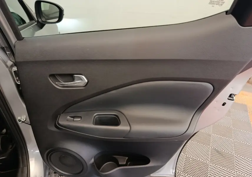 Vue intérieure de la porte avant gauche du Nissan Juke gris clair 2025, avec poignée et haut-parleur intégrés.