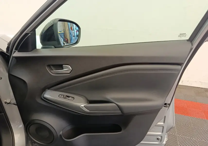 Vue intérieure de la porte avant gauche gris clair du Nissan Juke 2025 avec commandes de vitres et haut-parleur intégré.