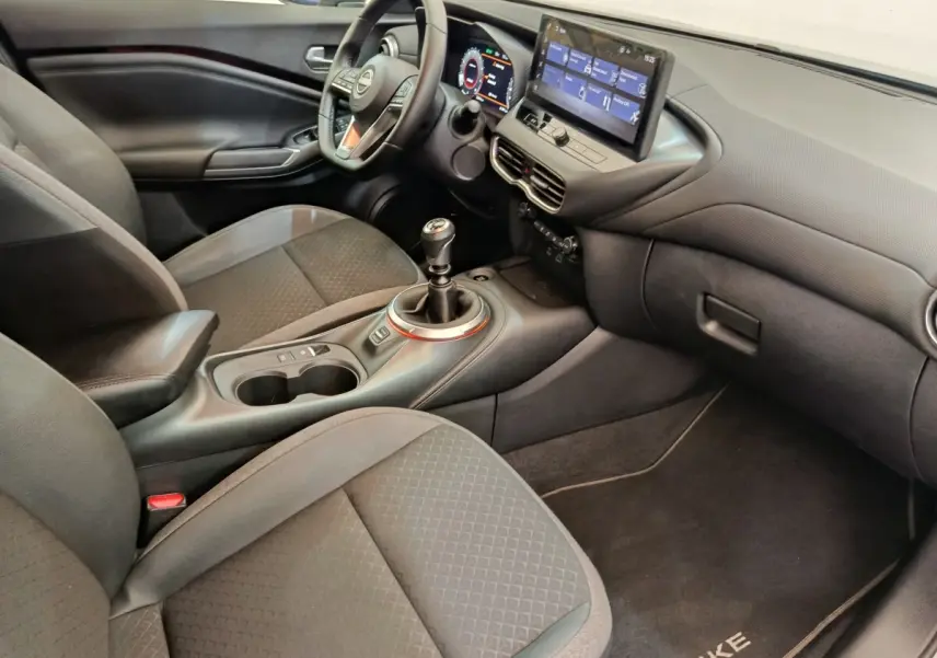 Intérieur avant droit du Nissan Juke gris clair 2025, volant multifonctions, écran tactile et boîte manuelle visible.