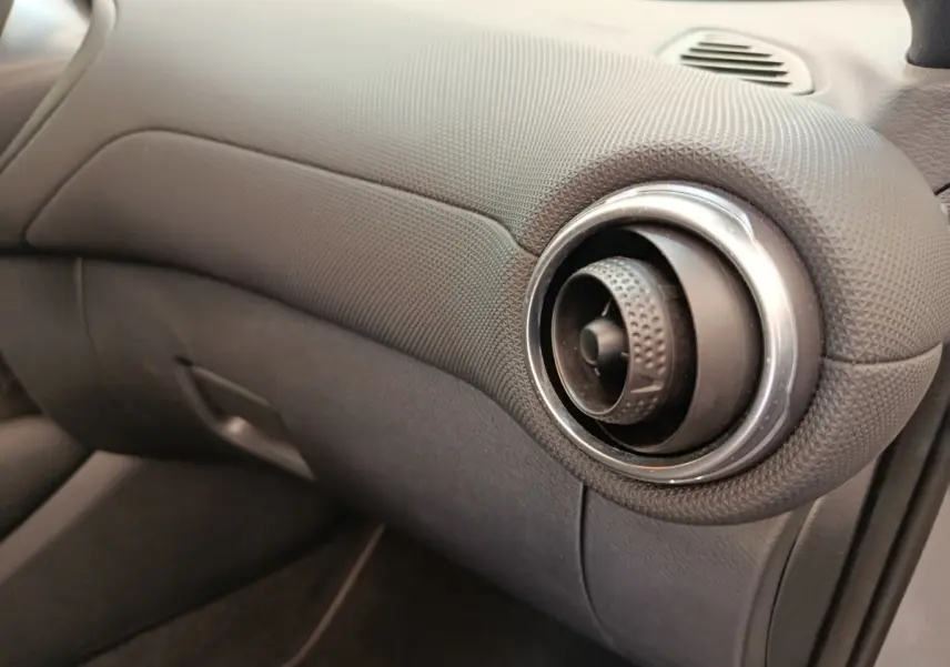 Détail de la sortie d'air ronde avec finition texturée du tableau de bord gris foncé du Nissan Juke 2025 côté passager.