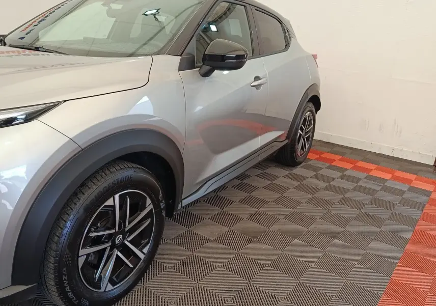 Vue 3/4 avant droit d'un Nissan Juke gris clair avec jantes noires et arches de roue noires contrastantes.