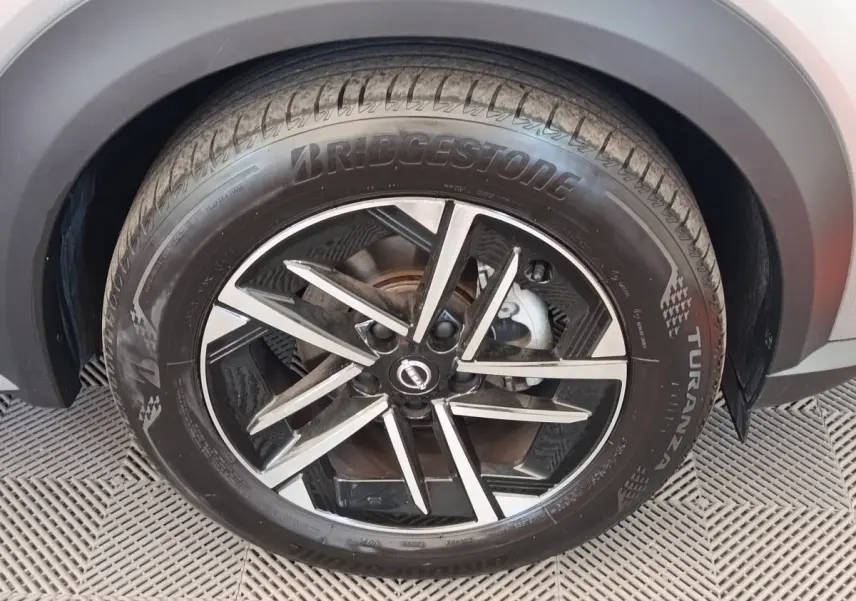Gros plan sur la roue avant droite du Nissan Juke gris clair, avec jante alliage noire et argentée au design moderne.