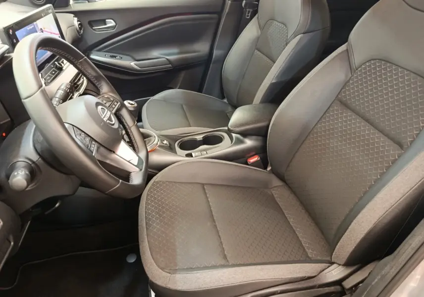Vue intérieure côté conducteur du Nissan Juke gris clair 2025, avec sièges tissu et volant multifonctions.