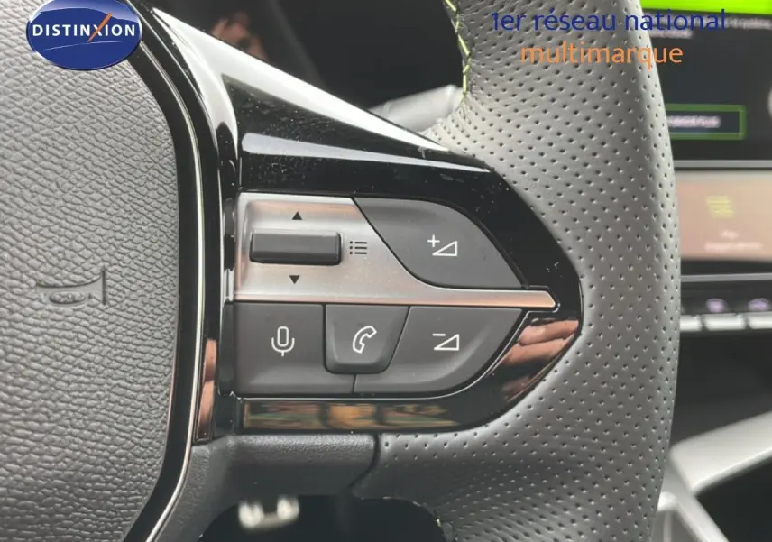 Gros plan sur les commandes à gauche du volant perforé d'une Peugeot 308 gris selenium 2026, avec boutons de volume et téléphone.