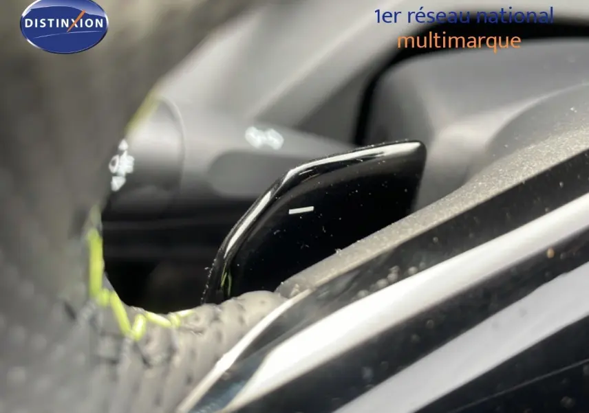 Gros plan sur la palette de changement de vitesse noire et brillante derrière le volant perforé d’une Peugeot 308 gris selenium.