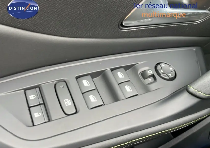 Gros plan sur la commande des vitres côté gauche d’une Peugeot 308 gris selenium, avec surpiqûres vertes visibles.