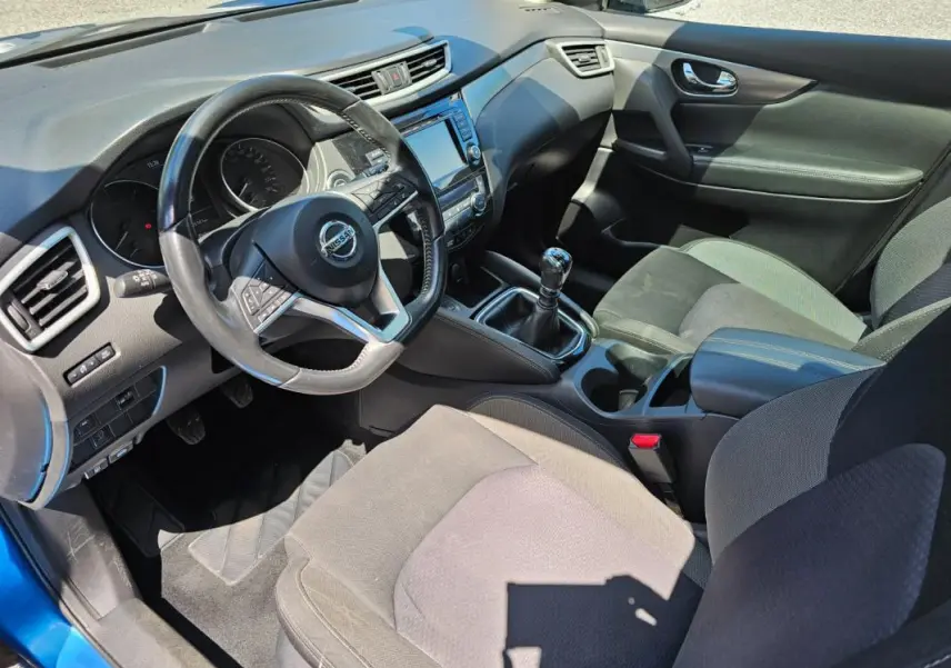 Vue intérieure côté conducteur du Nissan Qashqai bleu 2019, avec volant, tableau de bord et levier de vitesse manuel visibles.