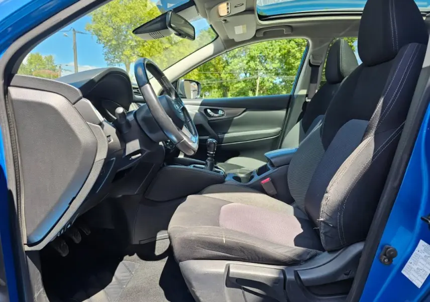 Intérieur côté conducteur du Nissan Qashqai bleu 2019, montrant le volant, la boîte manuelle et les sièges tissu noirs.