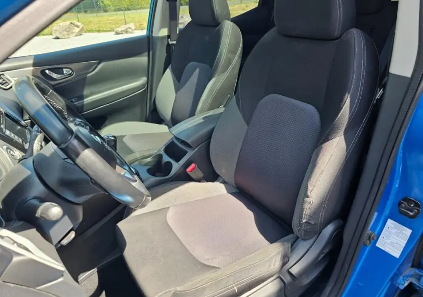 Vue intérieure côté conducteur du Nissan Qashqai bleu 2019, montrant les sièges en tissu noir et le volant.