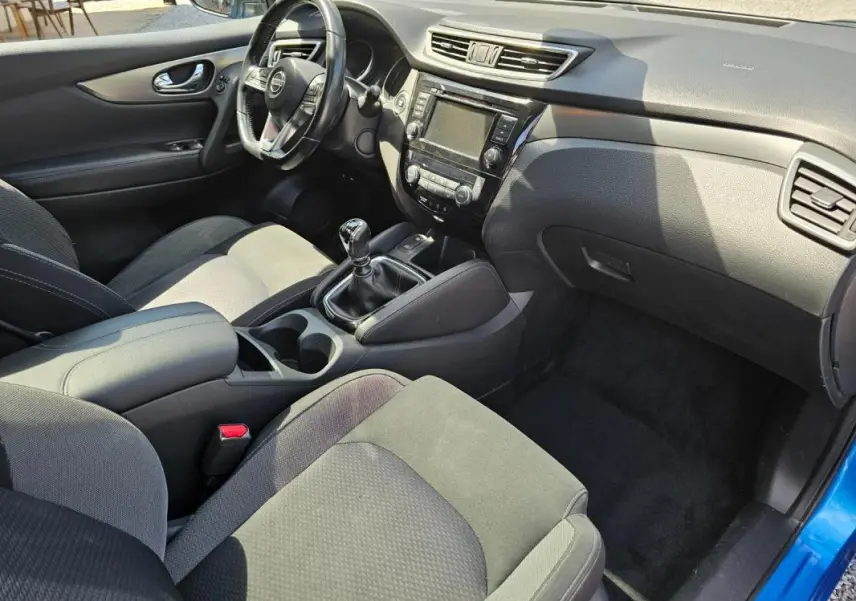 Vue intérieure côté conducteur du Nissan Qashqai bleu 2019, montrant le volant, la console centrale et la boîte manuelle.