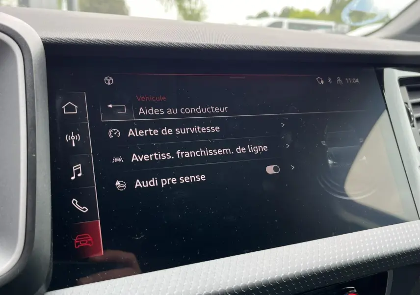 Écran tactile intérieur affichant les aides à la conduite de l'Audi A1 Sportback 25 TFSI rouge Misano, vue de face.