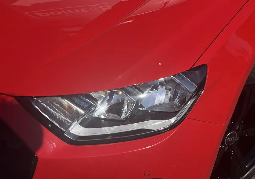 Gros plan sur le phare avant droit et la jante noire d'une Audi A1 Sportback rouge Misano, version 25 TFSI 95 Advanced.