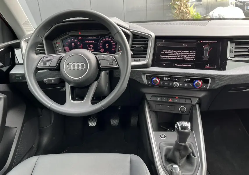 Vue intérieure avant de l'Audi A1 Sportback 2022 avec volant cuir, tableau de bord digital et levier de vitesse manuel.
