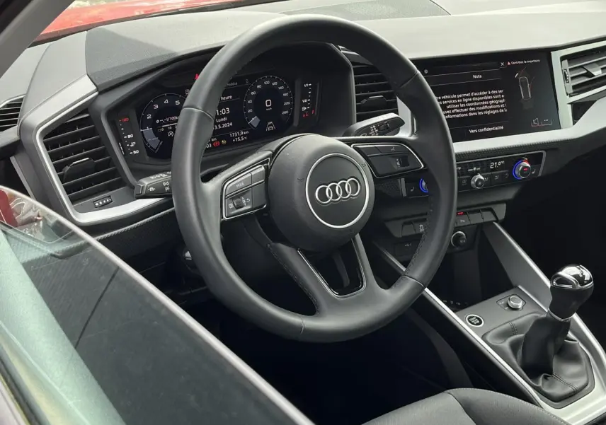 Vue intérieure côté conducteur de l'Audi A1 Sportback rouge Misano, volant cuir multifonctions et boîte manuelle visible.