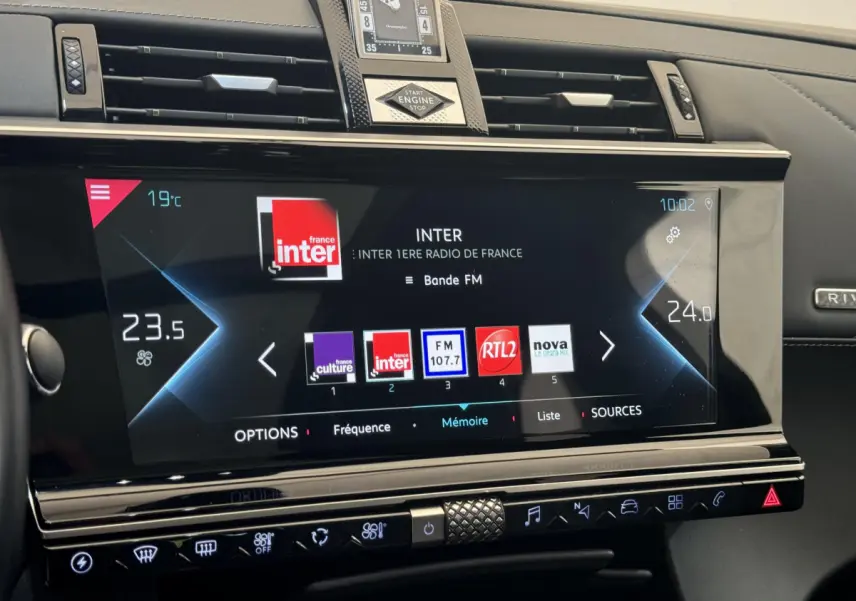 Vue rapprochée de l’écran tactile central du tableau de bord du DS7 Crossback bleu, affichant la radio FM et la climatisation digitale.