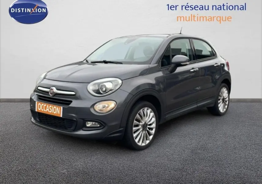 Fiat 500X gris foncé vue 3/4 avant droit, avec jantes alliage 18 pouces et phares antibrouillard allumés.
