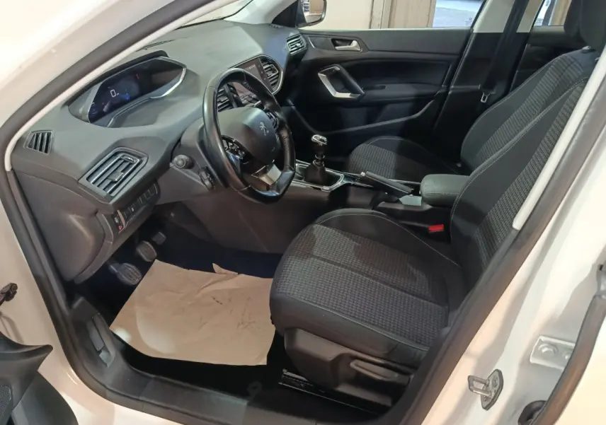 Intérieur côté conducteur d'une Peugeot 308 blanche 2021, volant cuir, sièges tissu noir et tableau de bord moderne.