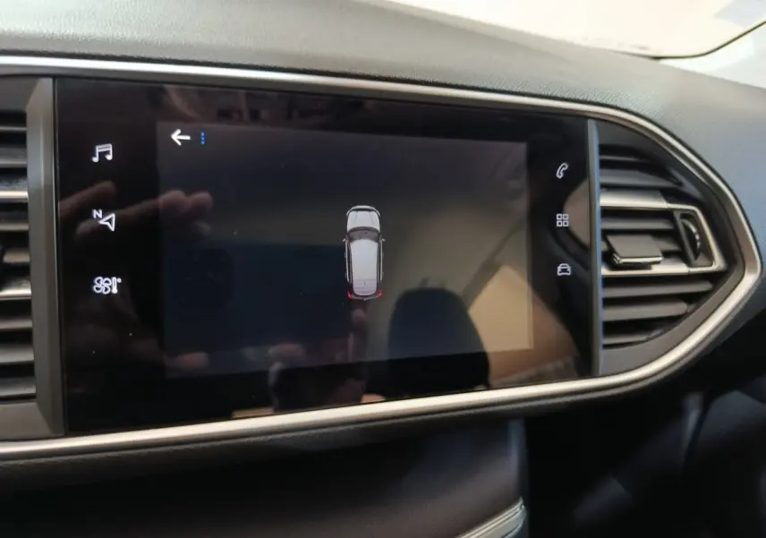 Écran tactile central affichant la vue aérienne du véhicule Peugeot 308 blanc, tableau de bord noir moderne.