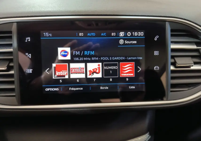 Écran tactile central de la Peugeot 308 blanc 2021 affichant les stations radio avec commandes autour en noir et beige.