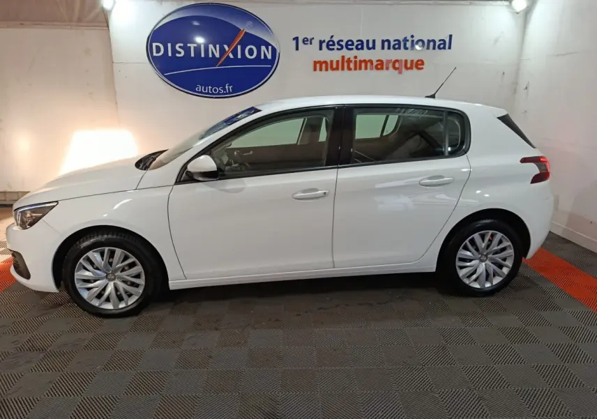 Profil côté gauche d'une Peugeot 308 blanche 2021, finition Premium Pack, dans un showroom avec logo Distinxion en arrière-plan.