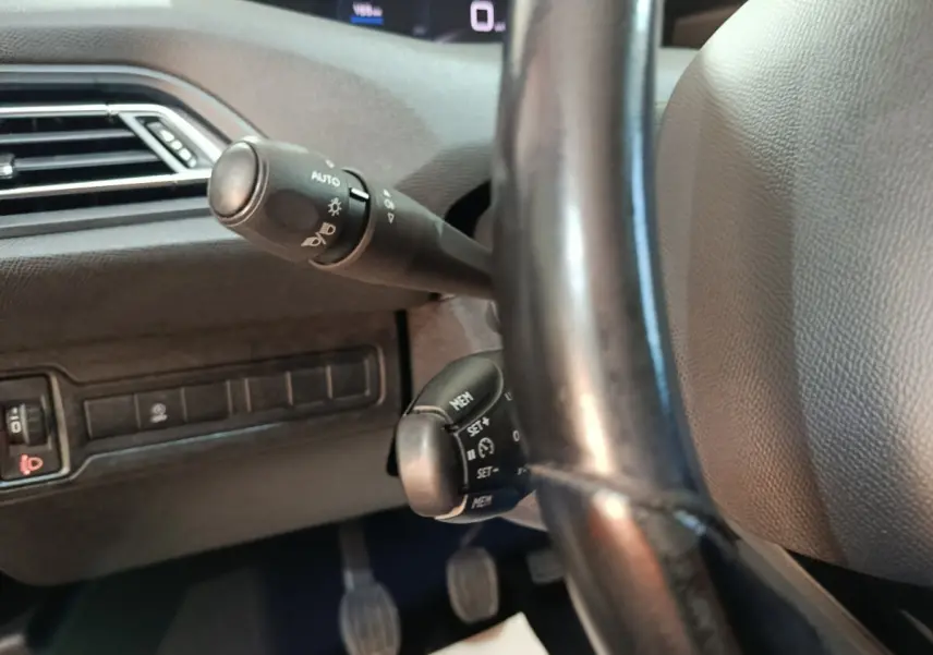 Gros plan sur la colonne de direction et commandes au volant cuir noir d'une Peugeot 308 blanche de 2021.