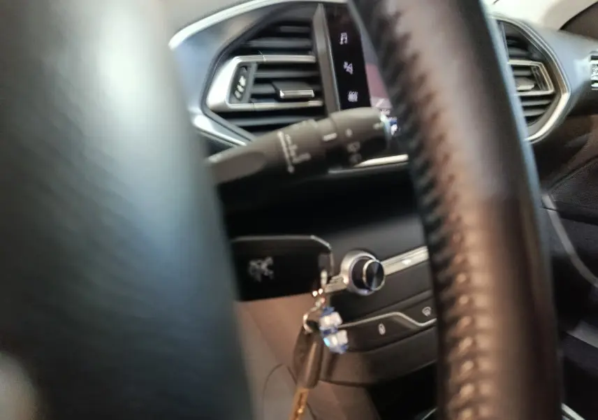 Intérieur de la Peugeot 308 2021 vu à travers le volant cuir, avec clé insérée et commandes du tableau de bord visibles.