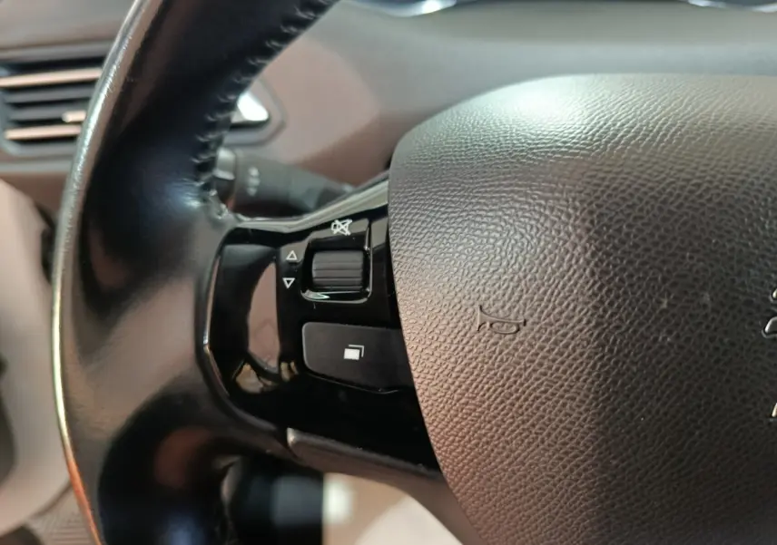 Gros plan sur la partie gauche du volant cuir de la Peugeot 308 blanc, avec commandes intégrées au volant.