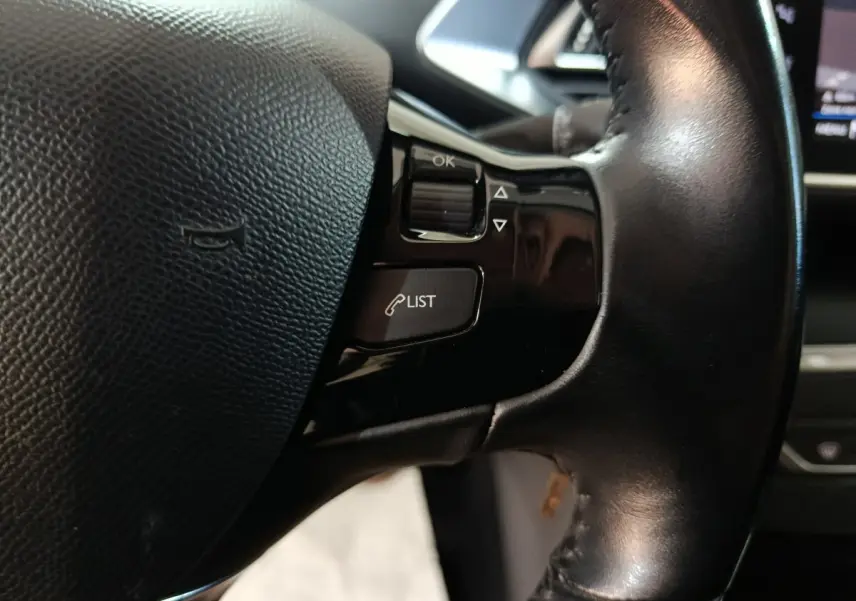 Gros plan sur le volant cuir noir de la Peugeot 308 BlueHDi 130, avec commandes vocales et boutons multifonctions visibles.