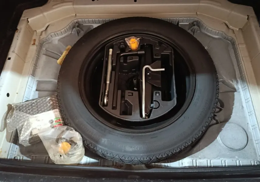 Vue de dessus du coffre ouvert d'une Peugeot 308 blanche, montrant la roue de secours et les outils de bord.