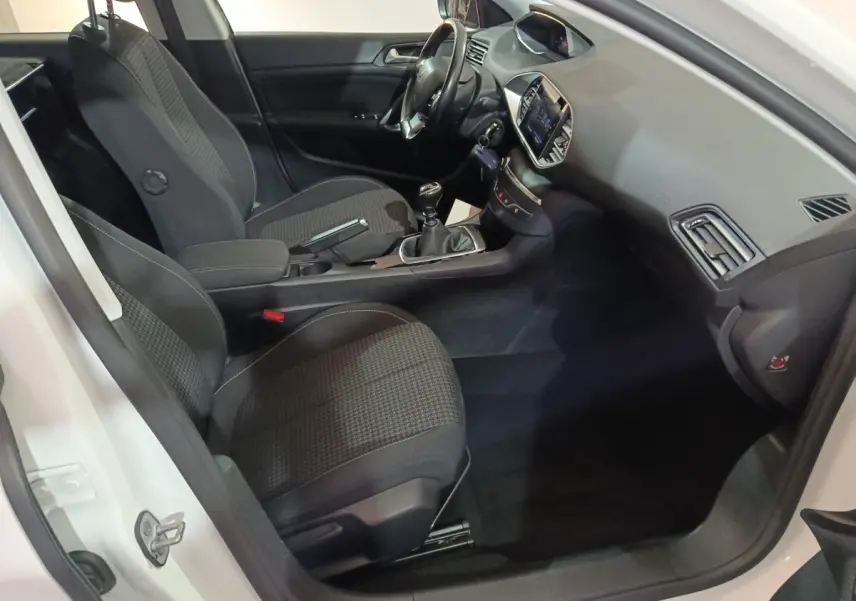 Vue intérieure côté conducteur de la Peugeot 308 blanche 2021, avec tableau de bord moderne et boîte manuelle.