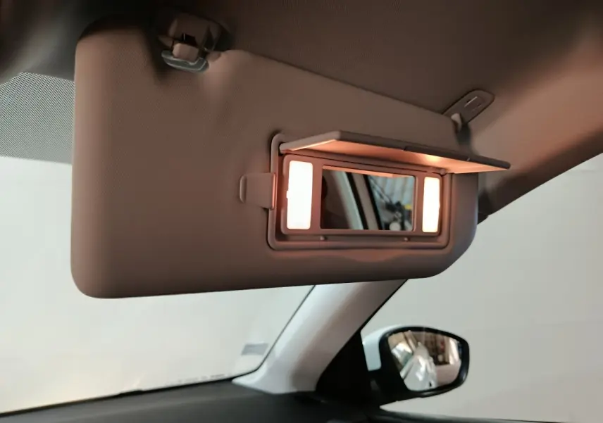 Miroir de courtoisie éclairé sur pare-soleil côté conducteur dans l'habitacle clair d'une Peugeot 308 blanche.