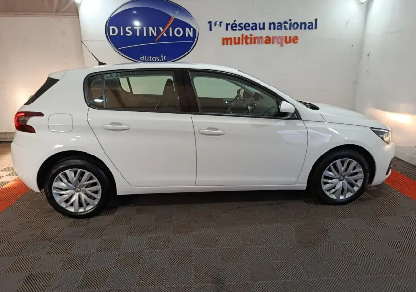 Profil droit d'une Peugeot 308 blanche 2021 dans un showroom avec logo Distinxion en arrière-plan.