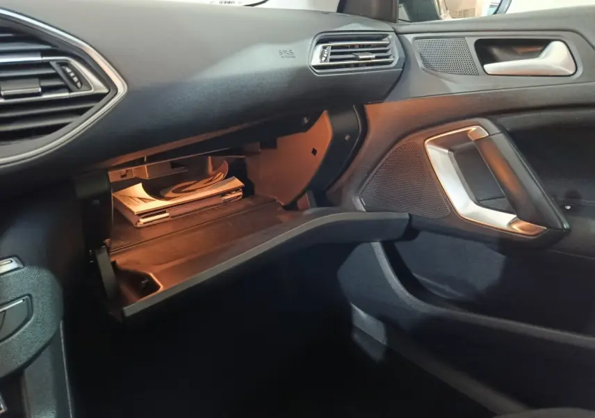 Intérieur noir de la Peugeot 308 2021, vue côté passager avec boîte à gants ouverte et poignée argentée.