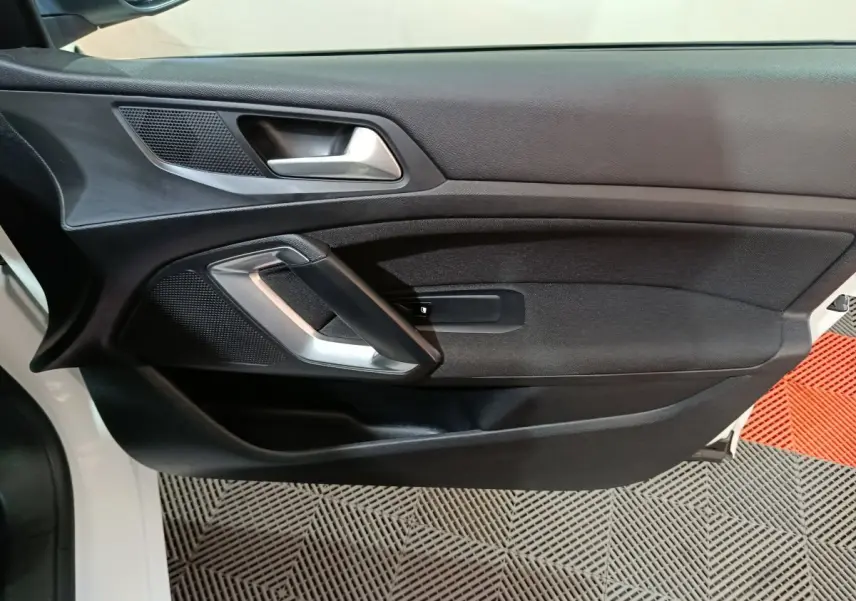 Vue rapprochée de la porte avant gauche noire de la Peugeot 308 blanche, avec poignée argentée et haut-parleur intégré.