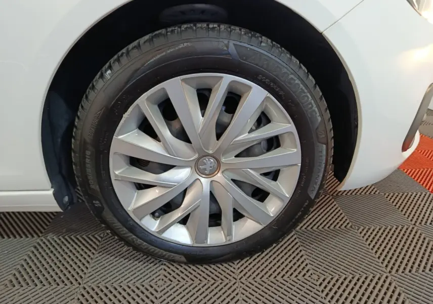 Gros plan sur la roue avant gauche d'une Peugeot 308 blanche, mettant en valeur la jante argentée au design moderne.