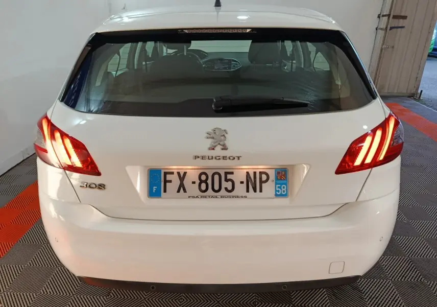 Vue arrière d'une Peugeot 308 blanche avec feux arrière allumés et plaque d'immatriculation française visible