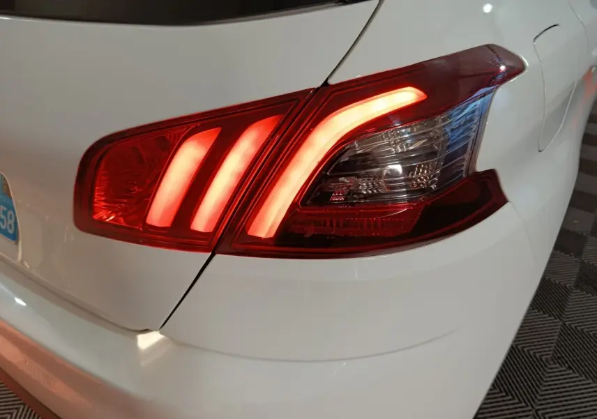Feu arrière droit allumé sur Peugeot 308 blanc, vue rapprochée du coin arrière du véhicule.